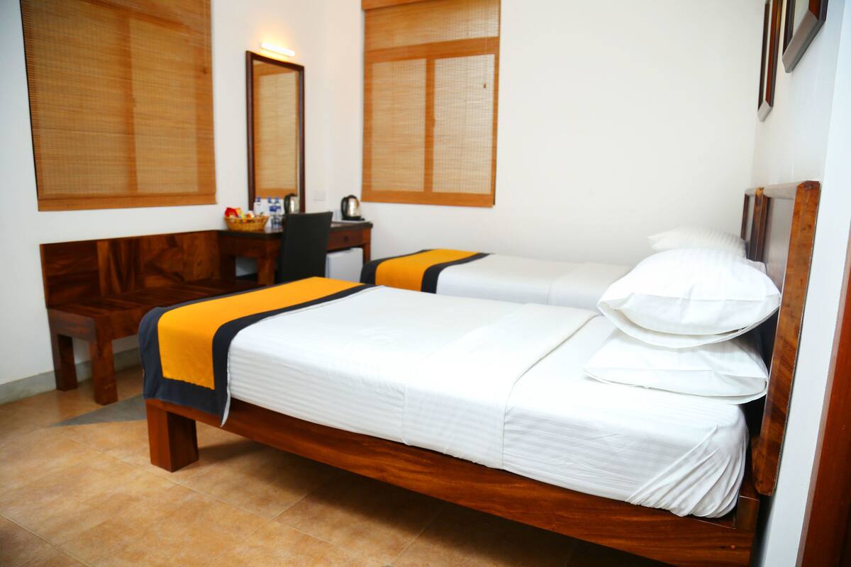 A hotel room with two beds, wooden headboards, a desk with a chair, and a mirror.