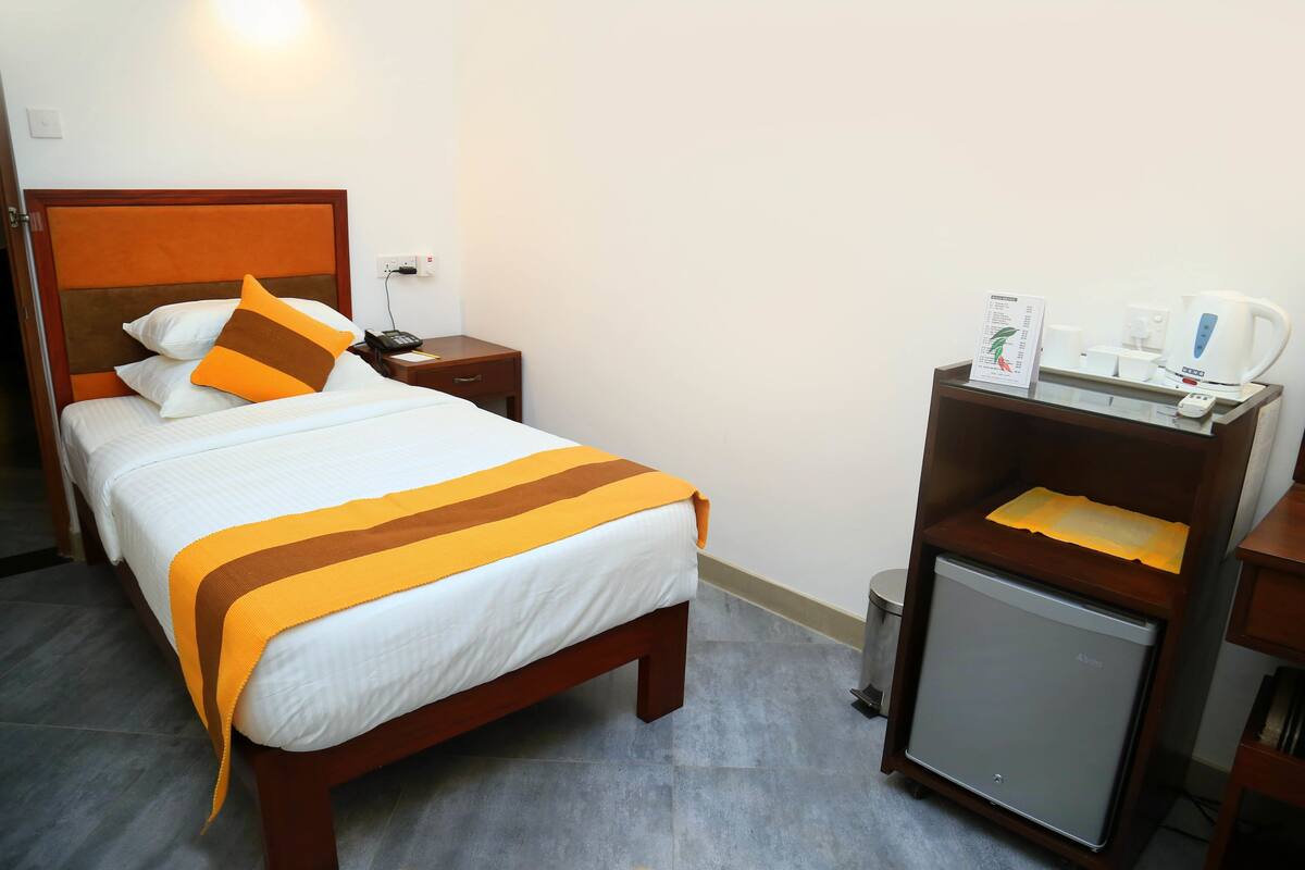 A hotel room with a bed, bedside table, and a small refrigerator.