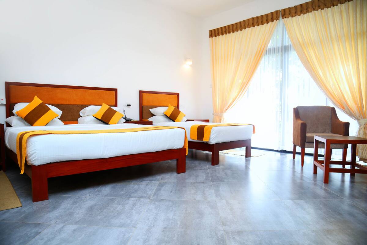 A hotel room with two beds, a chair, and a large window with curtains.