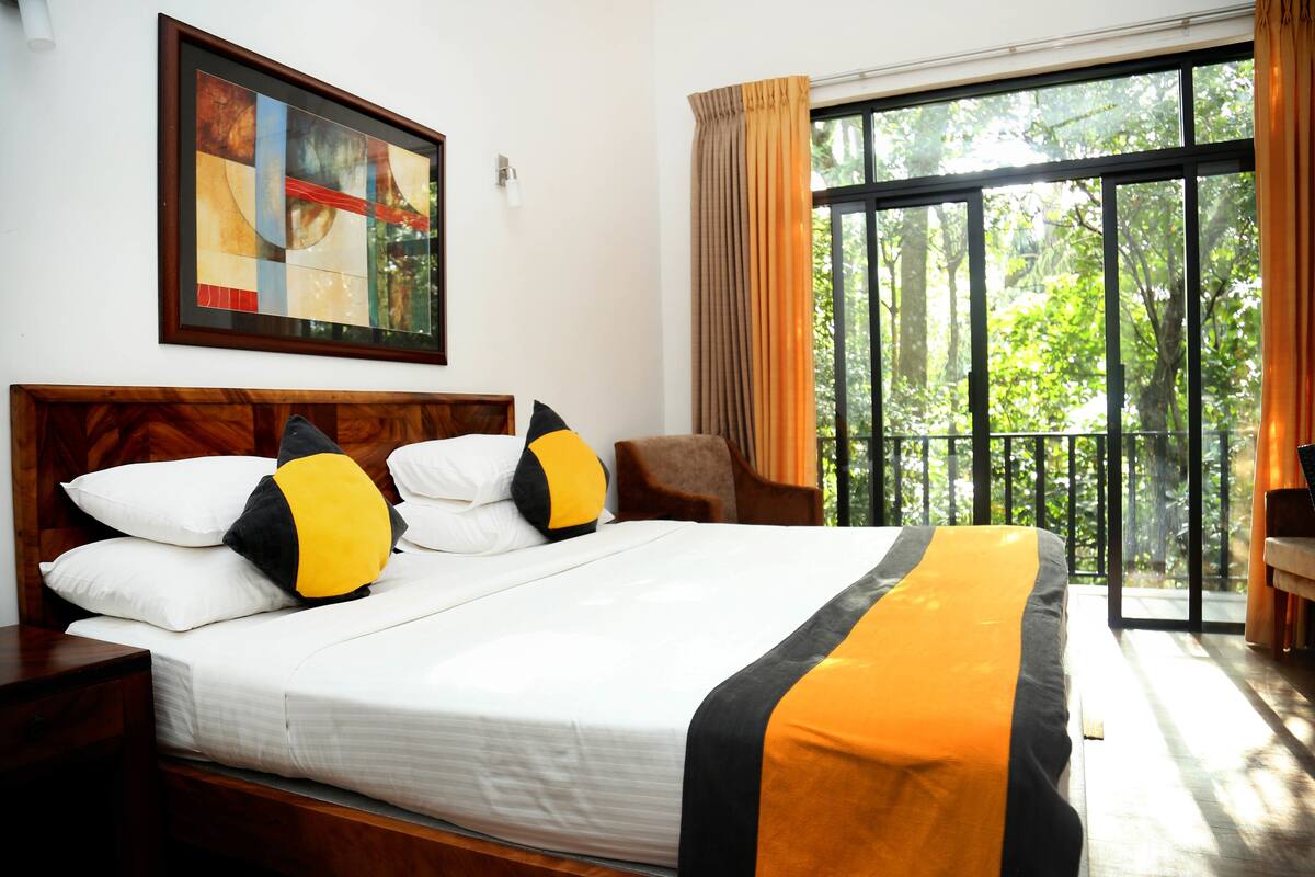A neatly made bed with white and black bedding, a wooden headboard, and a large window with curtains.