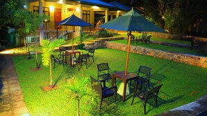 A well-lit outdoor area with a patio, chairs, and umbrellas, surrounded by a stone wall and greenery. - The Spring Villas (Kandy)