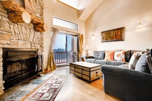 A living room with a stone fireplace, a sofa, a coffee table, and a view through a glass door.