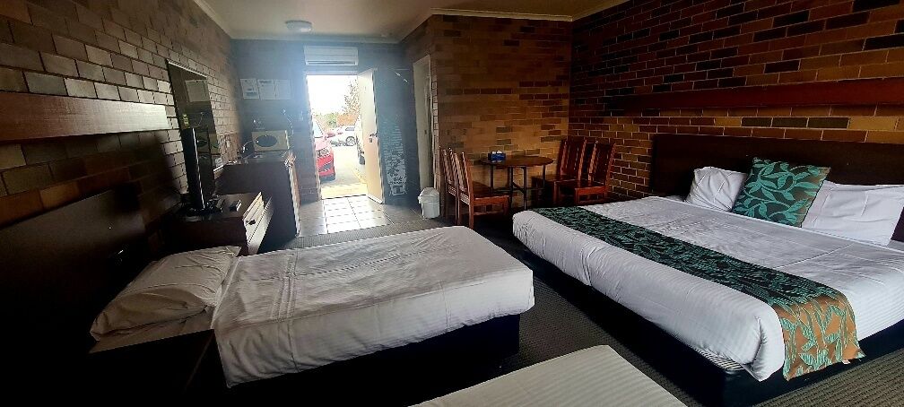 A hotel room with two beds, a brick wall, a small table with chairs, and a view of the outside.
