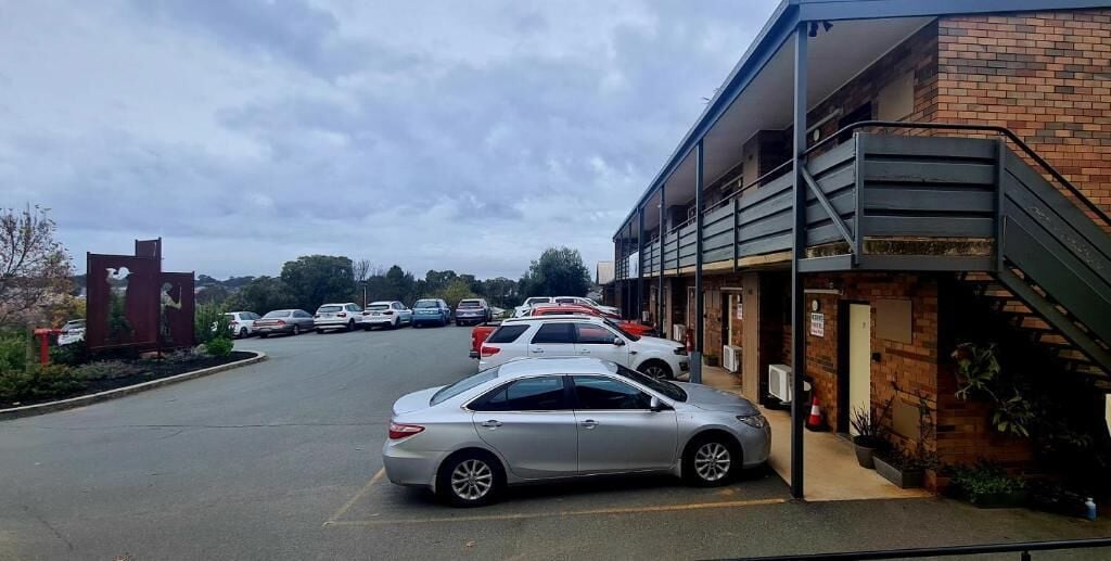 Ein Parkplatz mit mehreren Autos vor einem Gebäude mit Ziegelaußenwand und einer Treppe, die zu einer zweiten Etage führt.