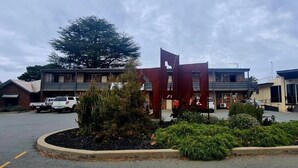 A parking lot with a building featuring a distinctive red and brown facade, surrounded by greenery and parked vehicles. - Shepparton Golf Club Motel (Shepparton)
