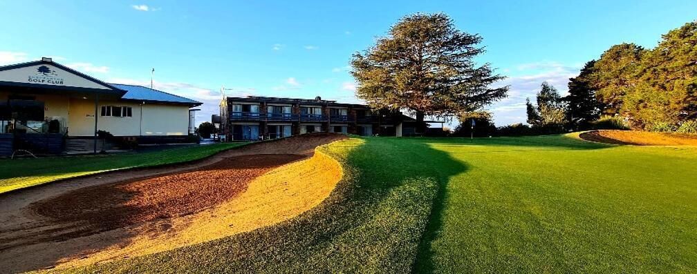 A golf course with a clubhouse, a large tree, and a clear sky.