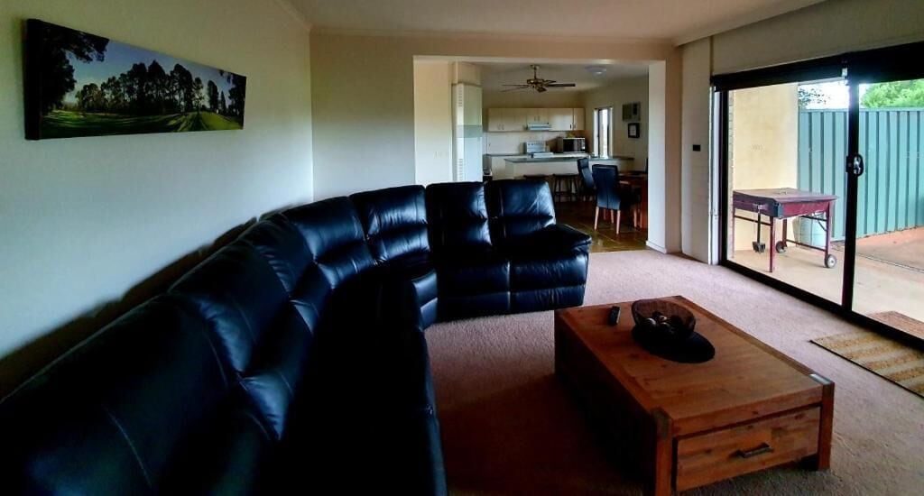 Sala de estar con sofá seccional, una mesa de centro de madera y vistas a una cocina y un patio.