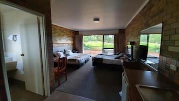 A hotel room with two beds, a kitchenette, a bathroom, and a view of the outdoors.