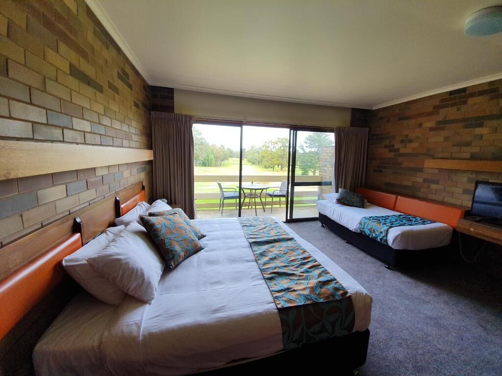 A hotel room with a large bed, a smaller bed, a desk with a computer, and a view of the outdoors through a sliding door.