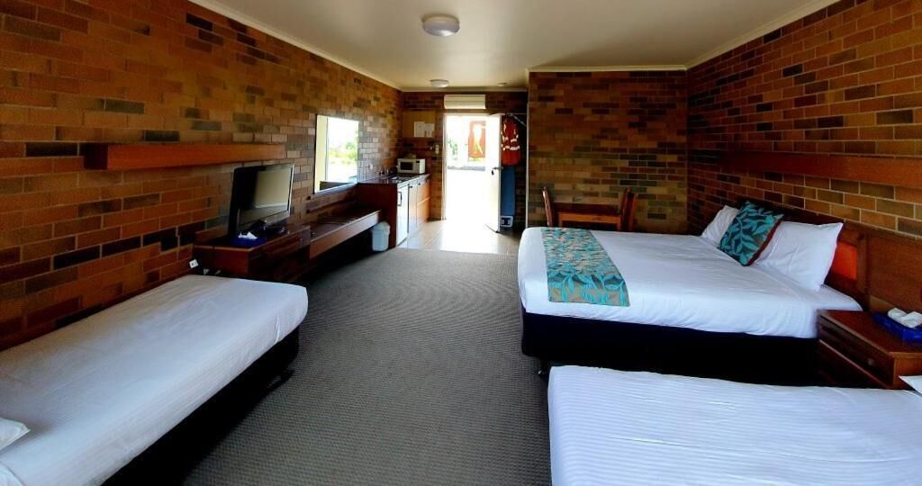 A hotel room with two single beds, a TV, a small kitchenette, and a brick wall.