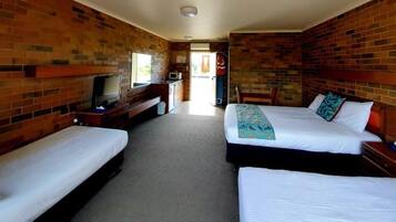 A hotel room with two single beds, a TV, a small kitchenette, and a brick wall.