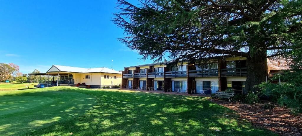 Un hotel con un área de estar cubierta al aire libre, un césped y un gran árbol.