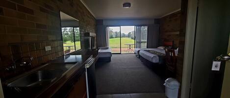 A hotel room with a kitchen area, a large window with a view of a grassy field, and a small table.