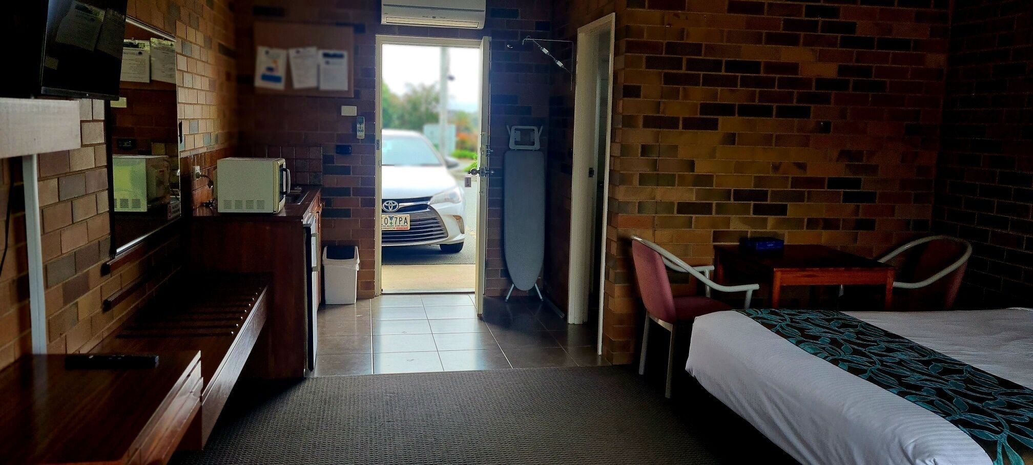 A hotel room with a bed, a desk, a chair, a television, and a view of the street outside.