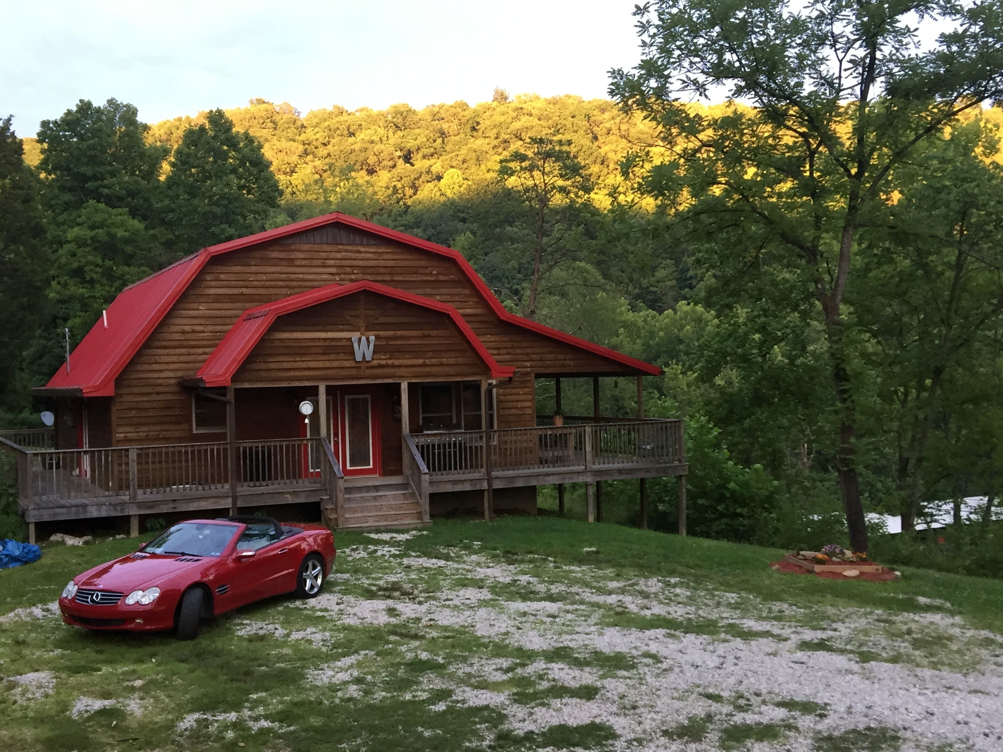 Een houten chalet met een rood dak, een veranda en een auto ervoor geparkeerd.