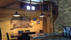 A rustic interior with wooden walls, a stone fireplace, a large fur rug, and a bar area.