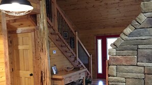 A wooden interior with a staircase, a stone wall, and a dining area.