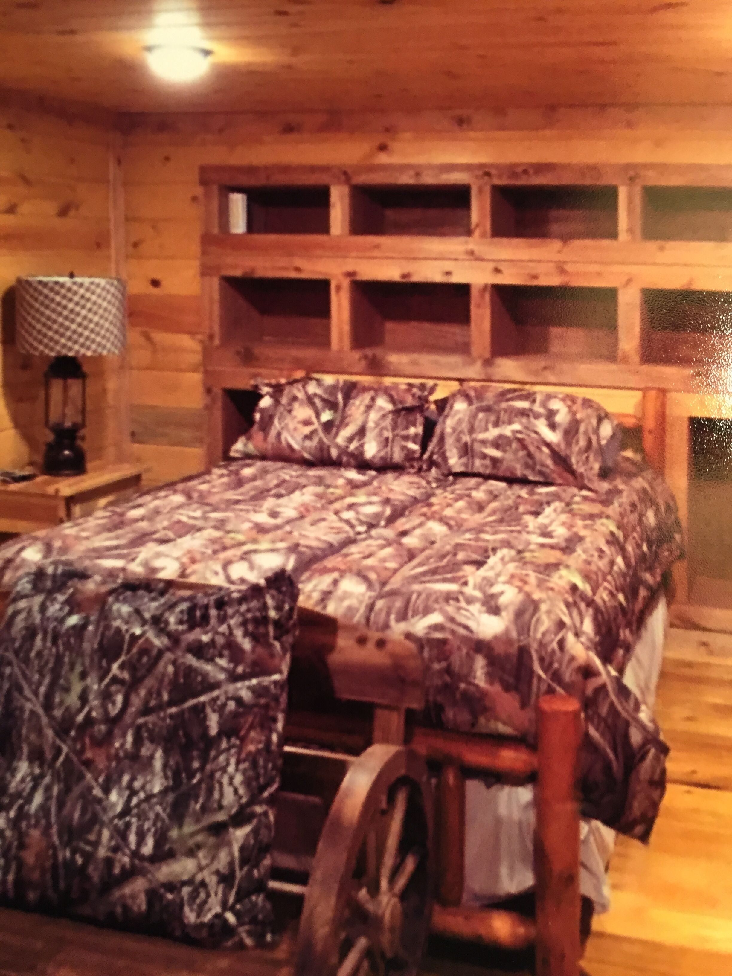Habitación de cabaña de madera con cama, lámpara y cabecera de madera con estantes.