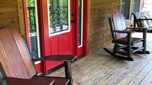 A wooden porch with red doors and a rocking chair.