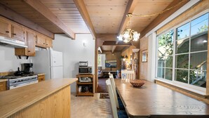 Una cocina con armarios de madera, una mesa de comedor con sillas, una lámpara de araña y un ventanal con vistas a zonas verdes.