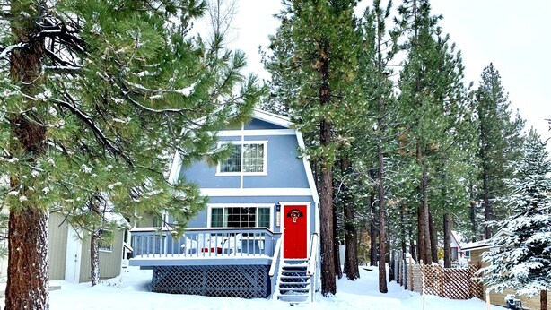 Una casa de dos pisos con una puerta roja, rodeada de árboles cubiertos de nieve y una valla de madera.