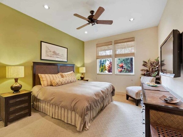 Un dormitorio con cama, mesitas de noche, escritorio, silla, ventilador de techo y ventanas con cortinas.