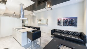 A modern kitchen with a central island, black leather sofa, and a cityscape painting on the wall.