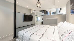A modern bedroom with a large bed, a flat-screen TV mounted on the wall, and a ceiling light fixture.