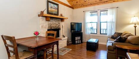 Ein gemütliches Wohnzimmer mit Holzbalkendecke, Kamin, Fernseher und einer Couch.