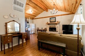 Una sala de estar acogedora con piso de madera, un sofá, un banco, una chimenea, un televisor y un comedor con mesa y sillas.