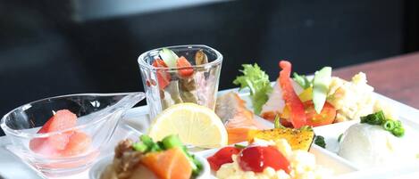 A white plate with various food items including salmon, vegetables, and a small glass of water.