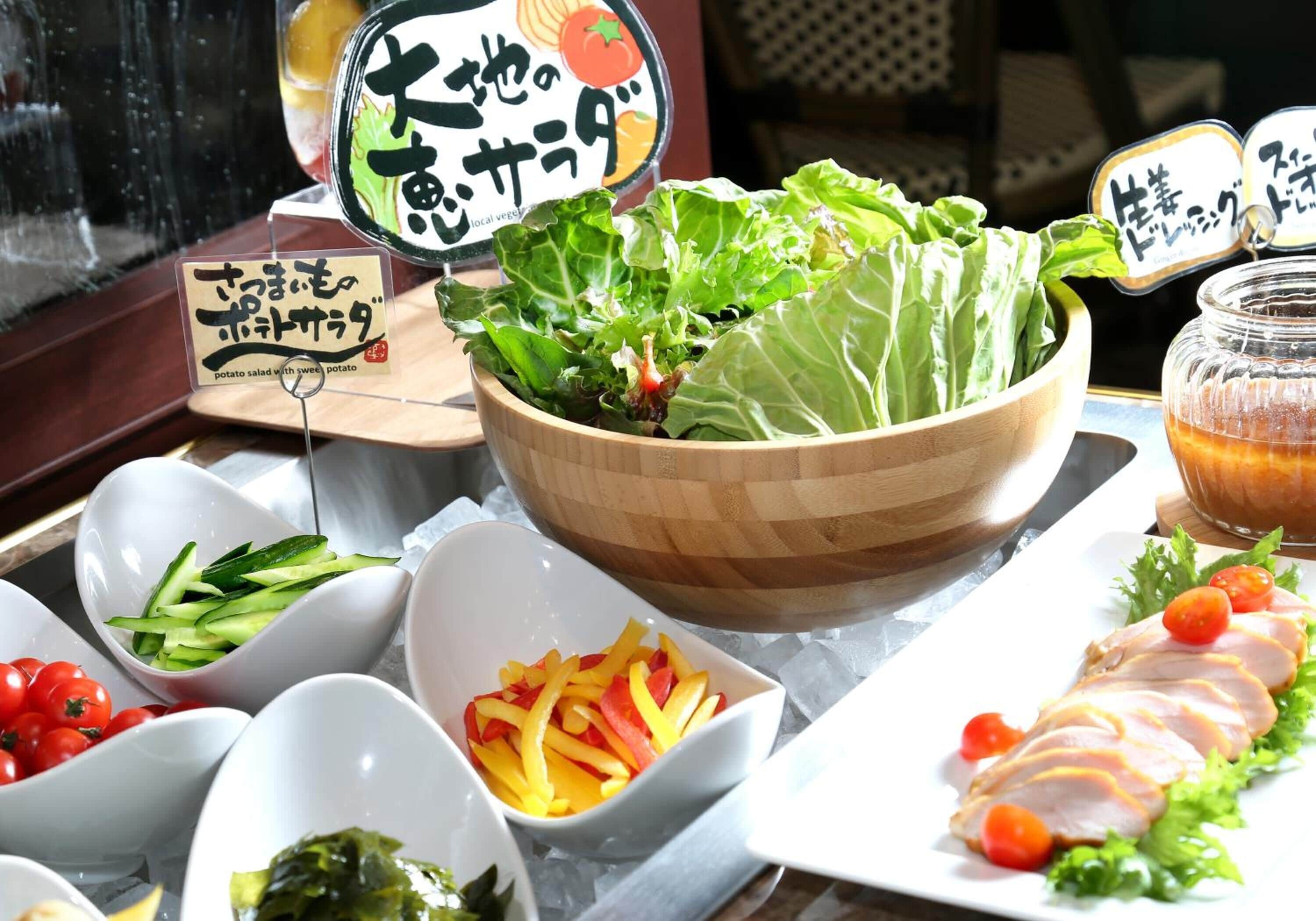 A variety of food items including a wooden bowl of lettuce, bowls of sliced vegetables, and a plate of sliced meat with cherry tomatoes.