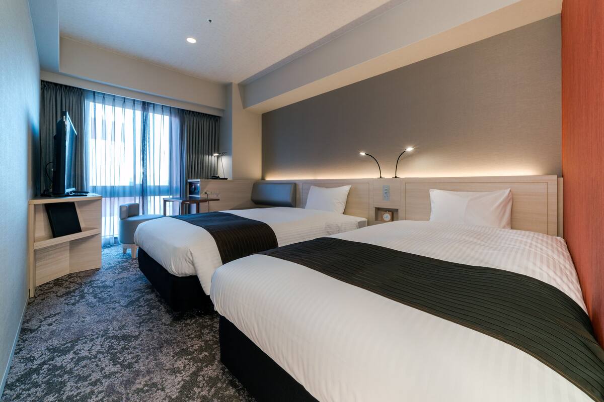 Ein Hotelzimmer mit zwei Betten, einem Schreibtisch, einem Stuhl und einem Fernseher.