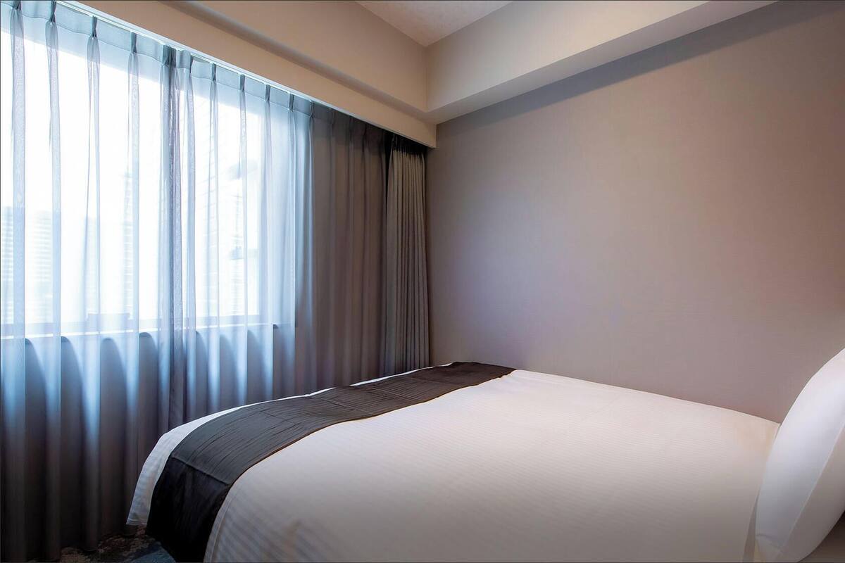 Ein Hotelzimmer mit einem Bett, Vorhängen und einer schlichten Wand.