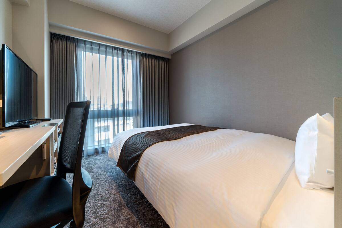 Ein Hotelzimmer mit Bett, Schreibtisch, Stuhl und Fernseher.
