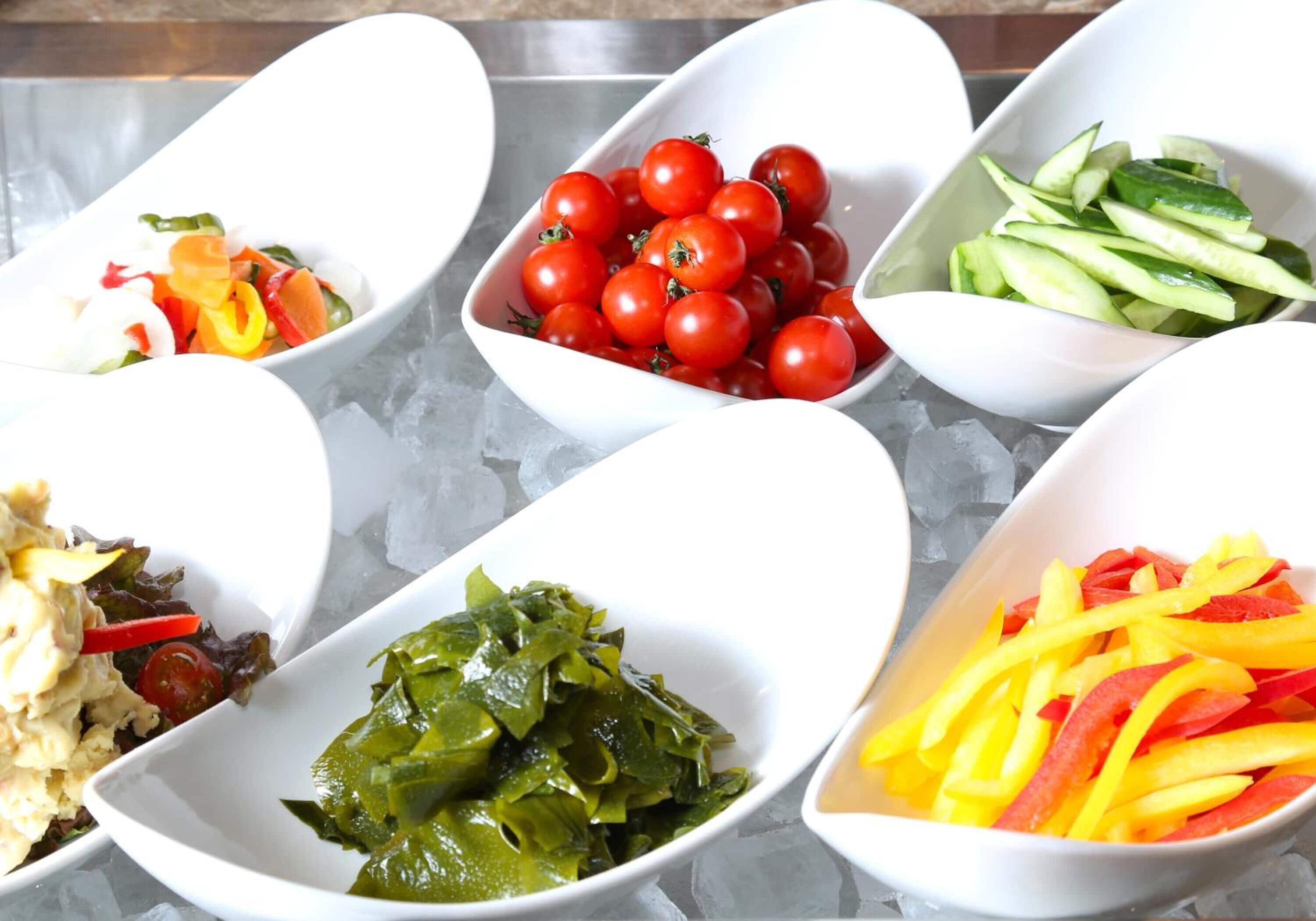 A variety of food items in white bowls on a table with ice.