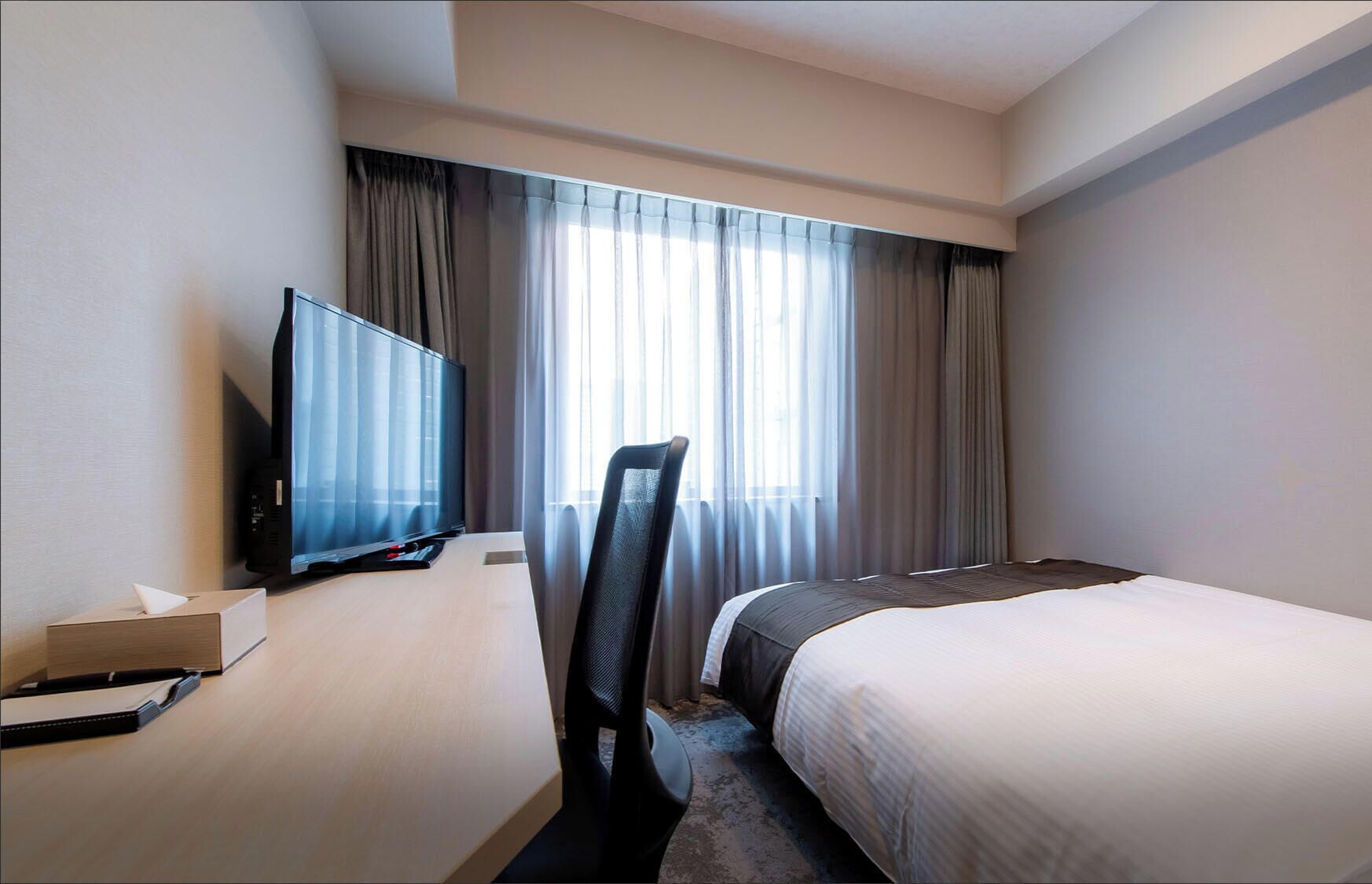 Et hotelværelse med seng, fjernsyn, skrivebord med computer og stol.