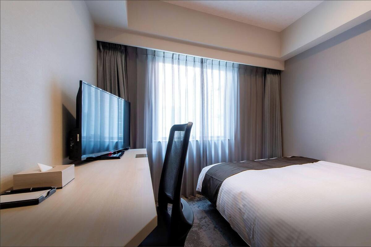 Ein Hotelzimmer mit einem Bett, einem Fernseher, einem Schreibtisch mit einem Computer und einem Sessel.