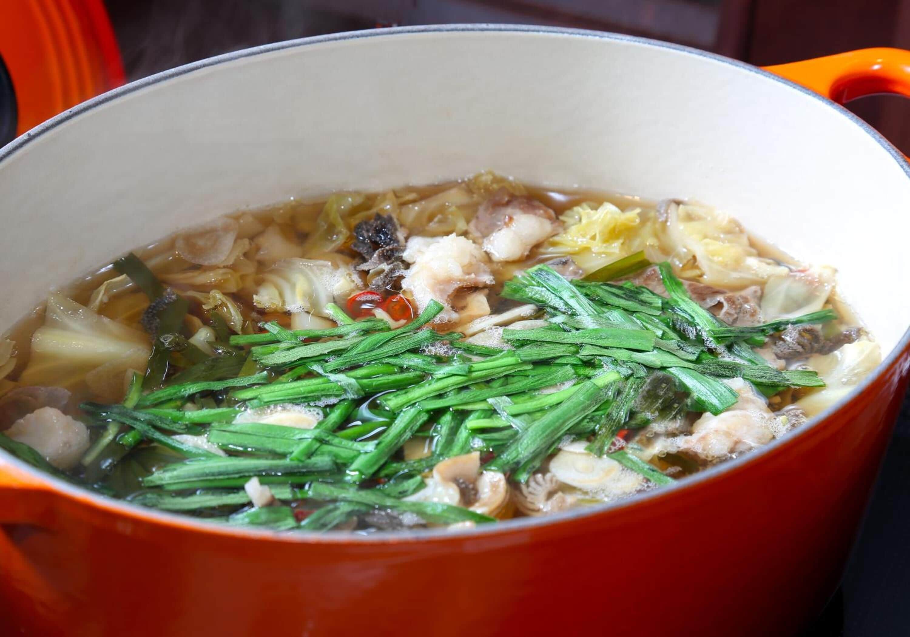 Una olla de sopa hirviendo con varios ingredientes, entre ellos cebollas verdes y champiñones.