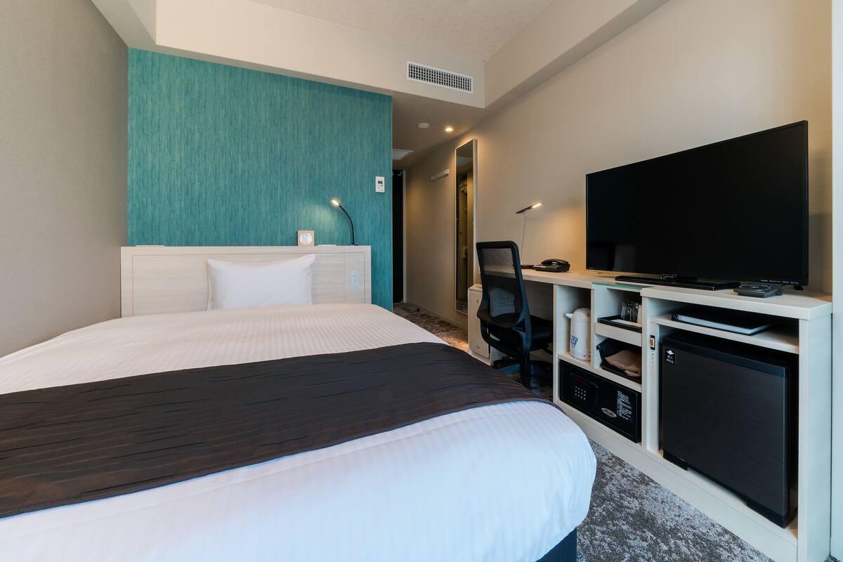 Ein Hotelzimmer mit einem großen Bett, einem Fernseher, einem Schreibtisch mit Computer und einer Minibar.