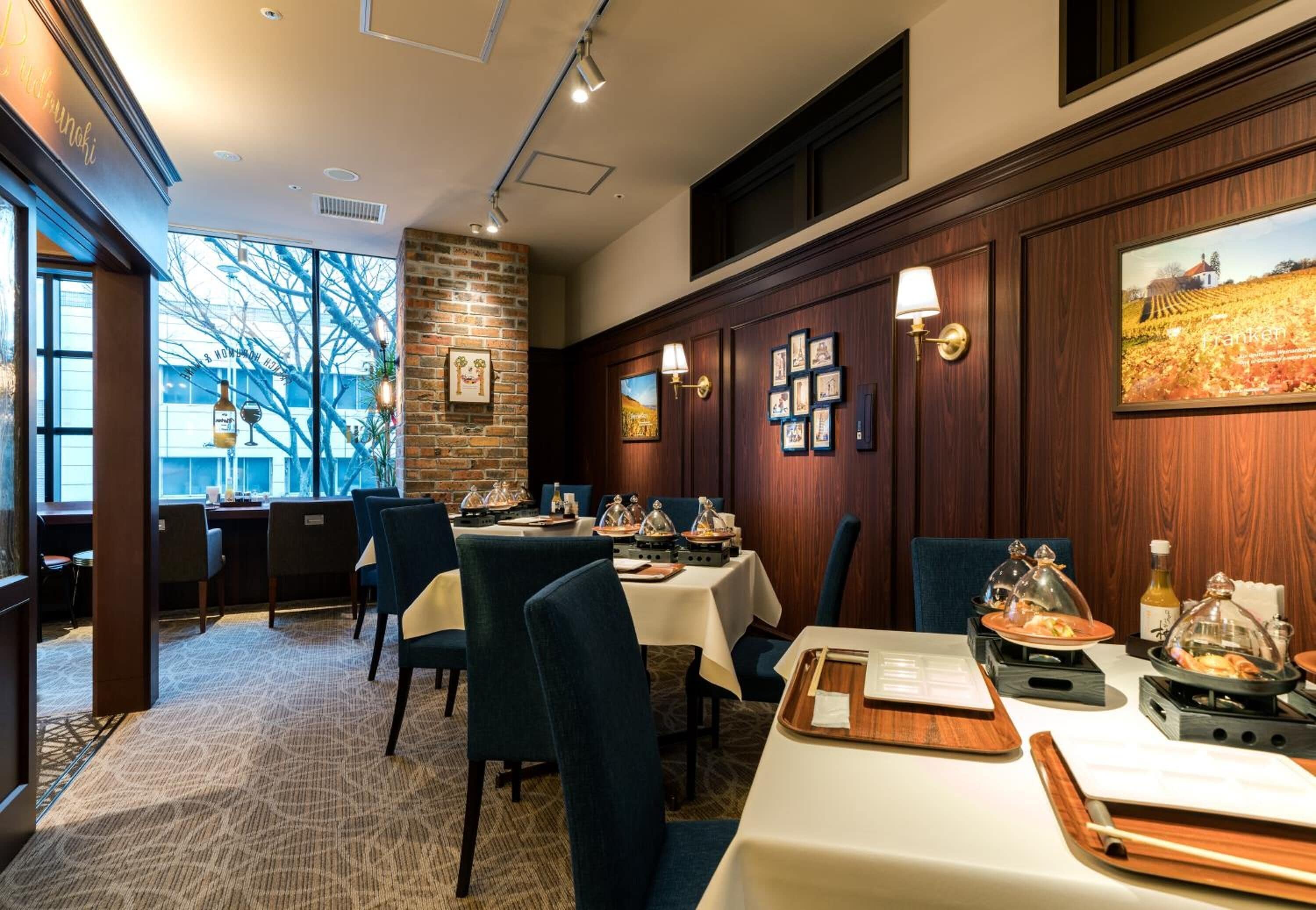 A restaurant with tables set for dining, a brick wall, and framed pictures on the wall.