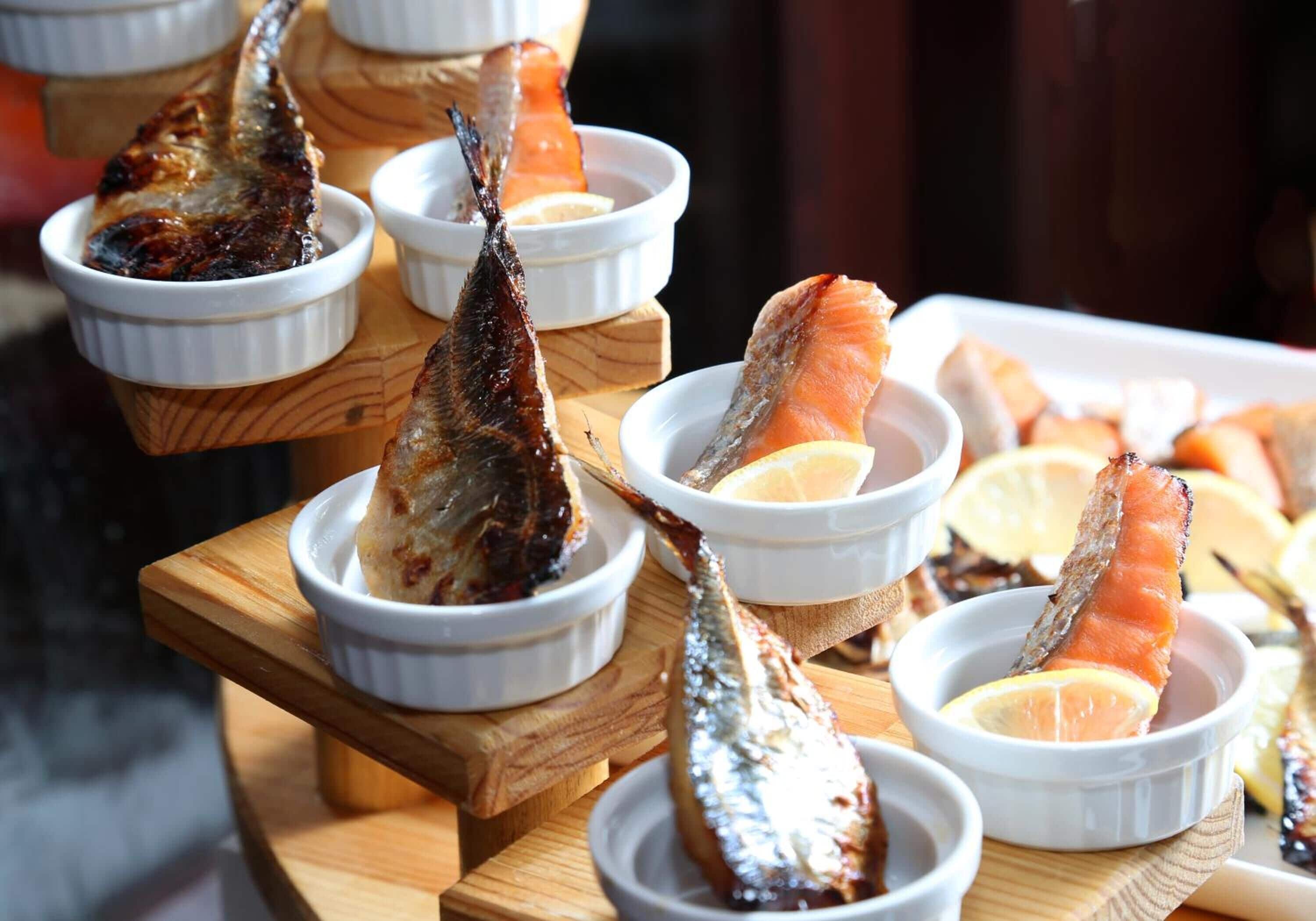 A wooden board with several white ramekins containing grilled fish and lemon slices.