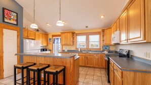 A kitchen with wooden cabinets, a central island with stools, a refrigerator, a microwave, and a sink. - Island Time - NH MP 11, 50 Ft to Beach, Elevator, Pool, Free Pool Heat, Hot Tub, Pets OK, YR Flex (Nags Head)