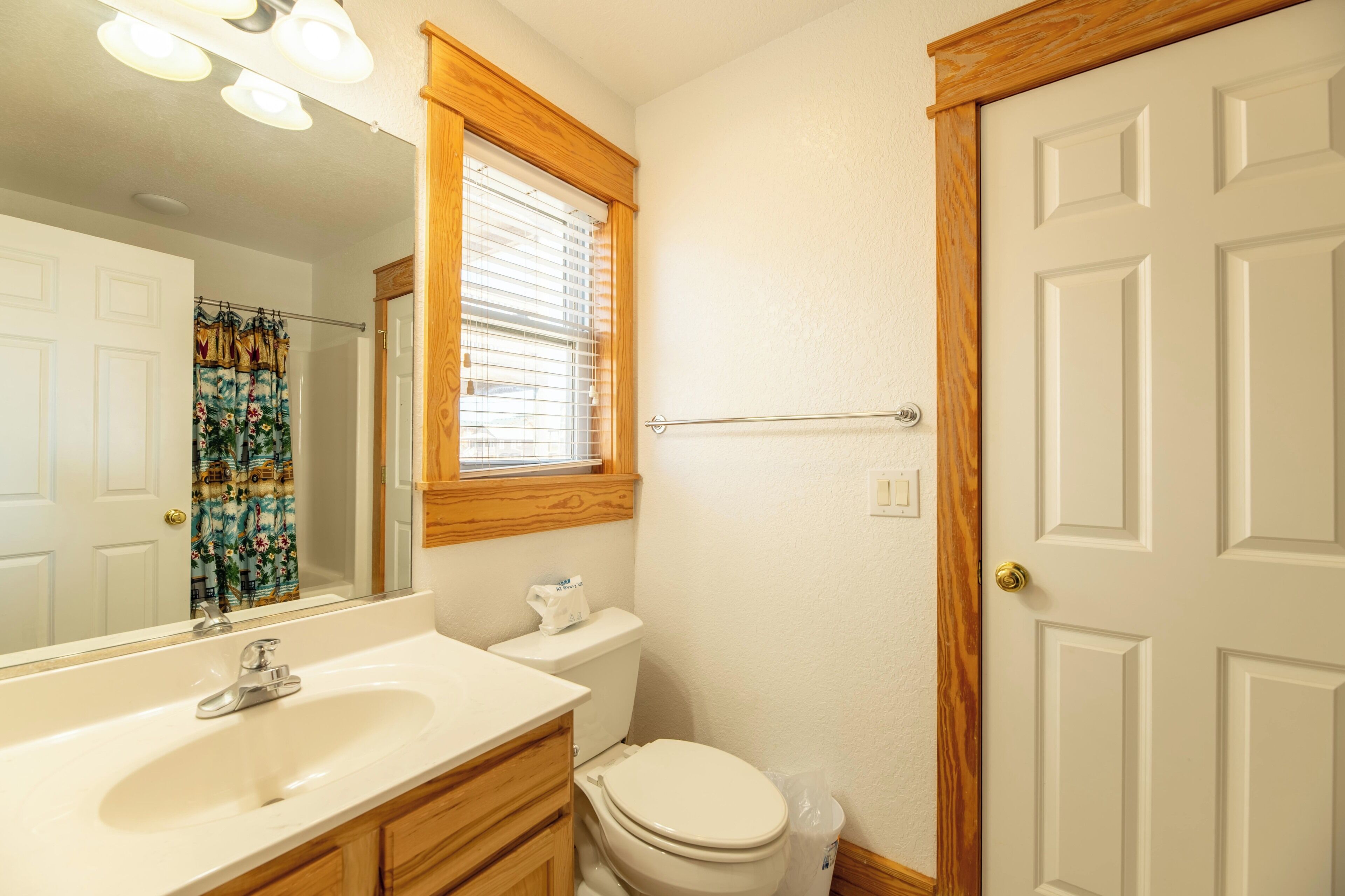 A bathroom with a white sink, wooden vanity, toilet, and a mirror.