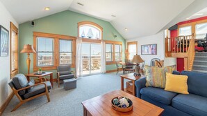 A spacious living area with a high ceiling, large windows, and a staircase leading to an upper level. - Island Time - NH MP 11, 50 Ft to Beach, Elevator, Pool, Free Pool Heat, Hot Tub, Pets OK, YR Flex (Nags Head)