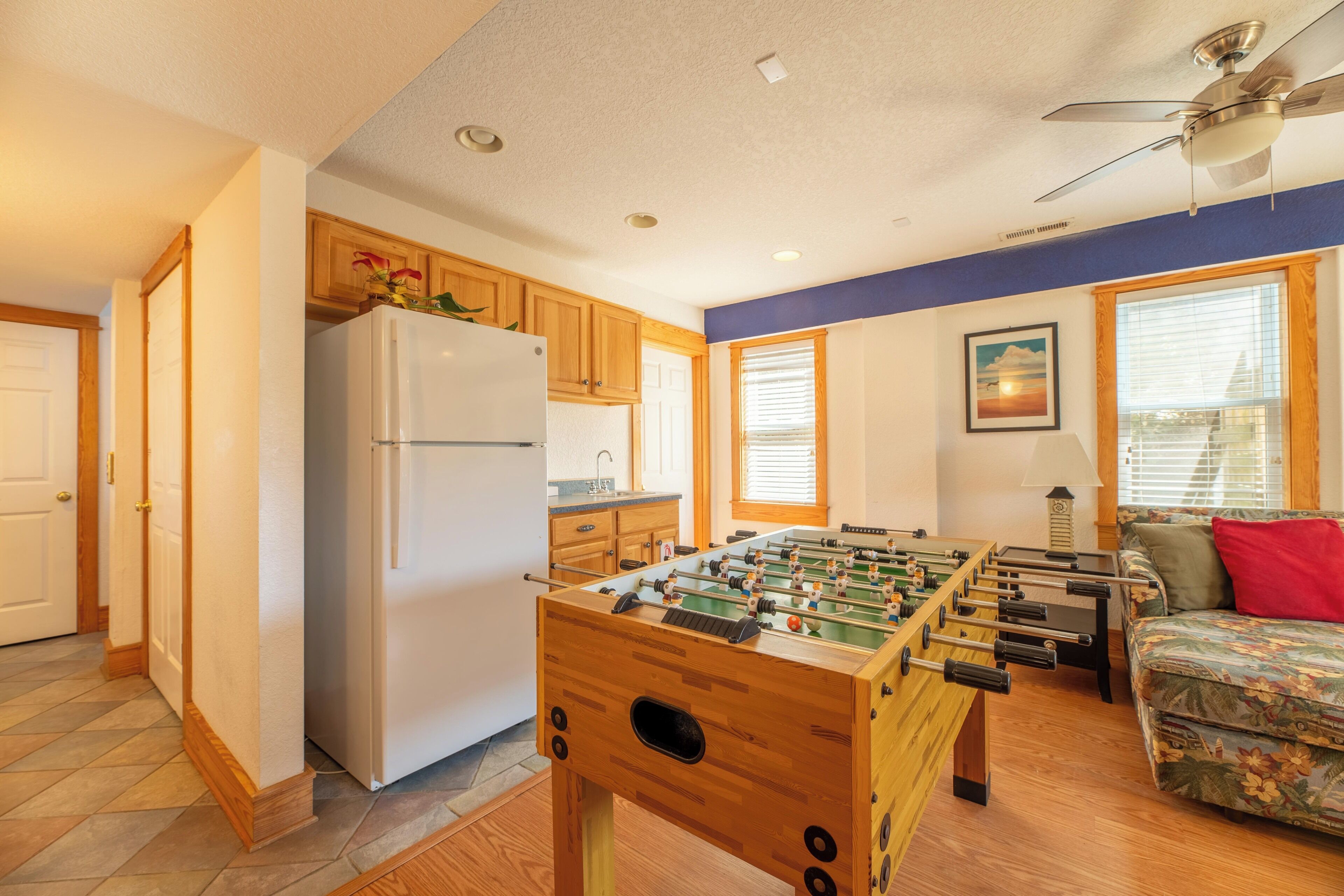 A kitchen with wooden cabinets, a white refrigerator, a foosball table, and a ceiling fan.