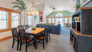 A spacious living area with a dining table, chairs, a sofa, and a fireplace. - Island Time - NH MP 11, 50 Ft to Beach, Elevator, Pool, Free Pool Heat, Hot Tub, Pets OK, YR Flex (Nags Head)
