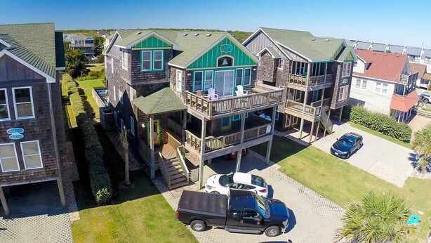 A multi-story residential building with a balcony, a driveway, and a parked truck. - Island Time - NH MP 11, 50 Ft to Beach, Elevator, Pool, Free Pool Heat, Hot Tub, Pets OK, YR Flex (Nags Head)