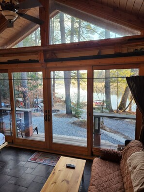 Interior d'una cabana acollidora, amb un gran finestral corredís que dona a una terrassa, una taula de fusta i una zona de seients confortable.