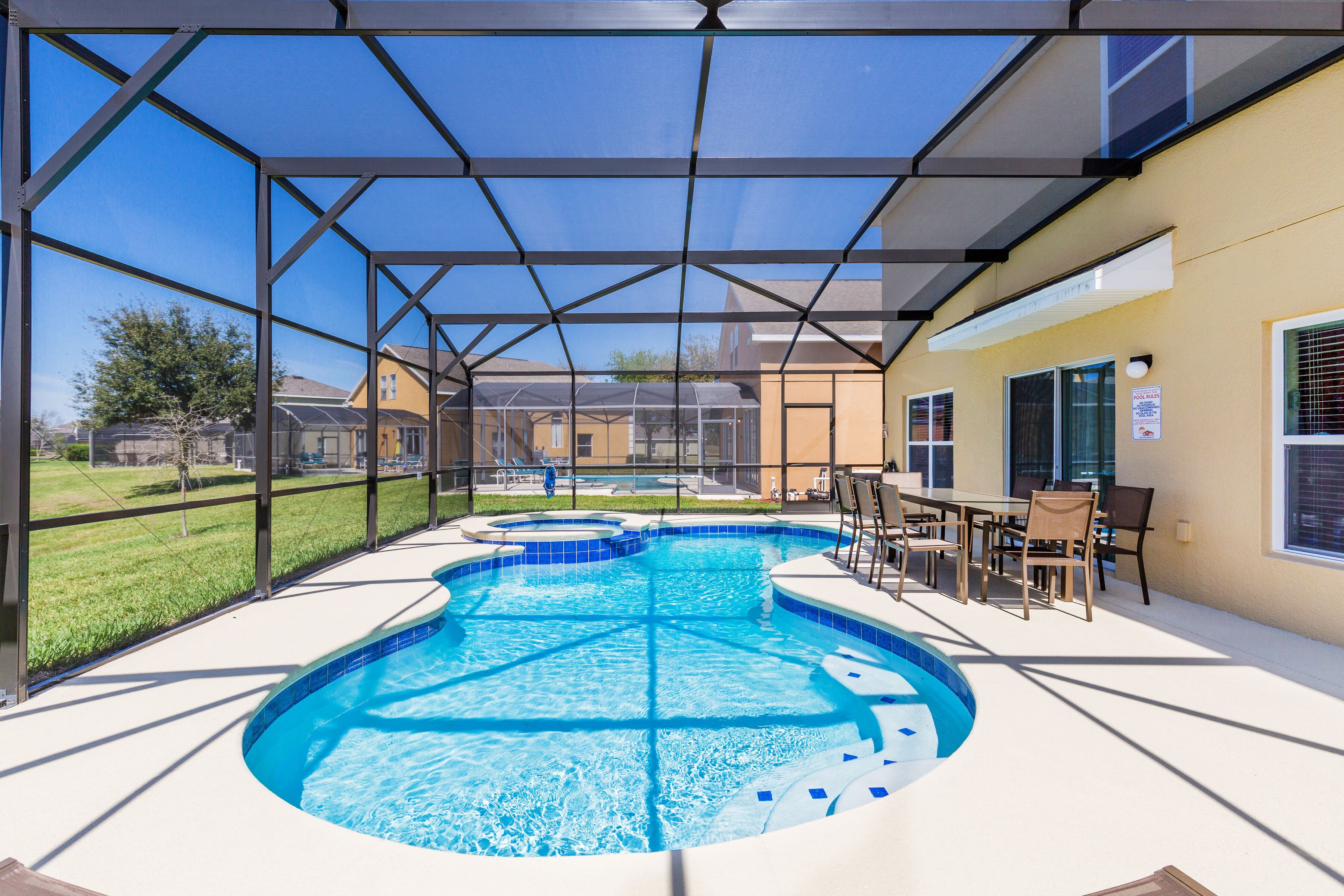 Une piscine entourée d’une structure en verre, elle-même bordée d’une terrasse avec des chaises et une table.
